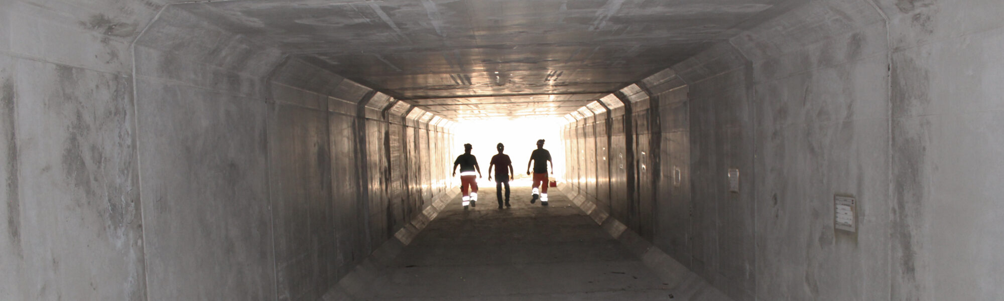 3 personer går gennem en beton-tunnel.